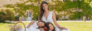 Woman in white dress and two children sitting on grass in a serene garden setting, symbolizing elegance and tranquility.