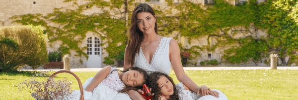 Woman in white dress and two children sitting on grass in a serene garden setting, symbolizing elegance and tranquility.