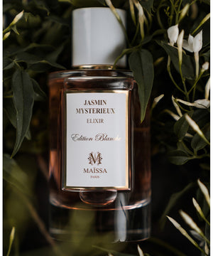 Exquisite bottle of JASMIN MYSTERIEUX by Maison Maïssa surrounded by jasmine leaves, from the5thscent fragrance collection.