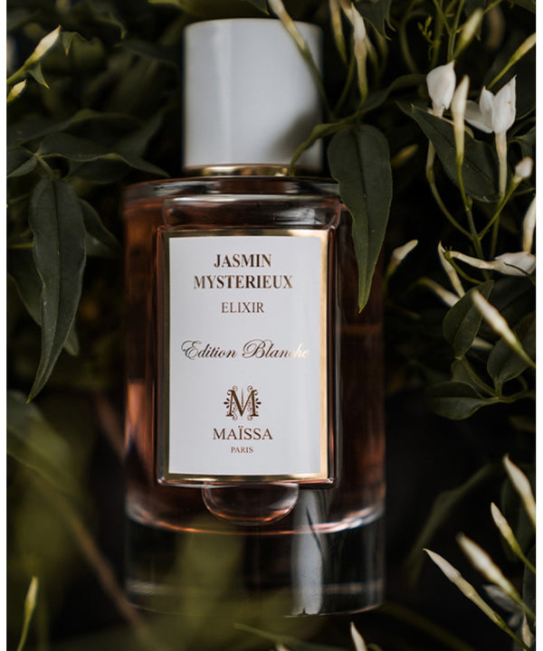 Exquisite bottle of JASMIN MYSTERIEUX by Maison Maïssa surrounded by jasmine leaves, from the5thscent fragrance collection.