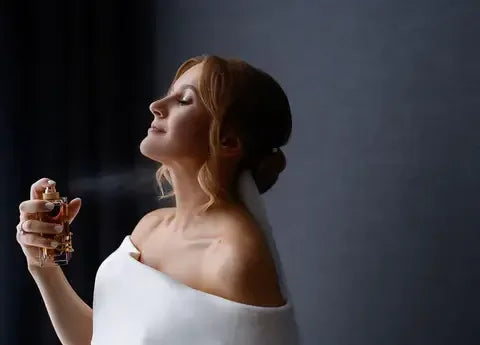 Young woman with closed eyes spraying perfume on neck against dark background