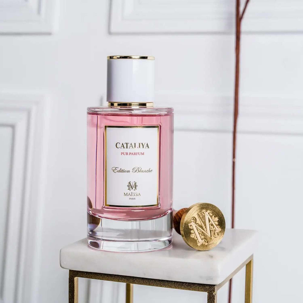 Pink Cataliya perfume bottle with white cap and gold accents on marble stand