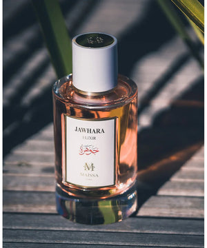 Jawhara Elixir perfume bottle by Maissa with pink liquid on wooden surface in natural light
